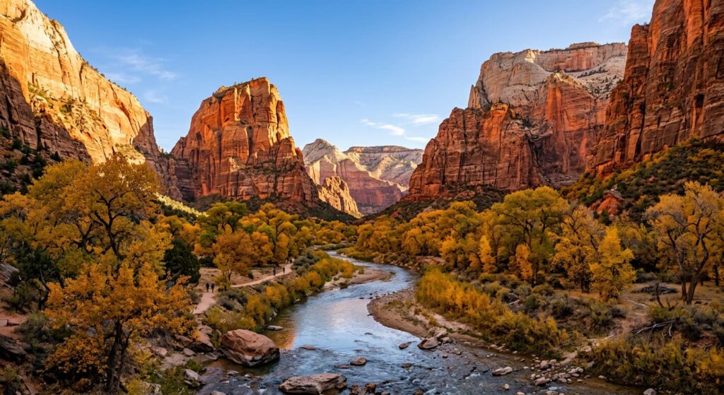Zion Canyon from the canyon floor looking north, towering Navajo sandstone walls in warm orange-red morning light, Virgin River winding through cottonwood trees in October gold, dramatic scale of canyon walls against blue sky, Utah Southwest landscape photography