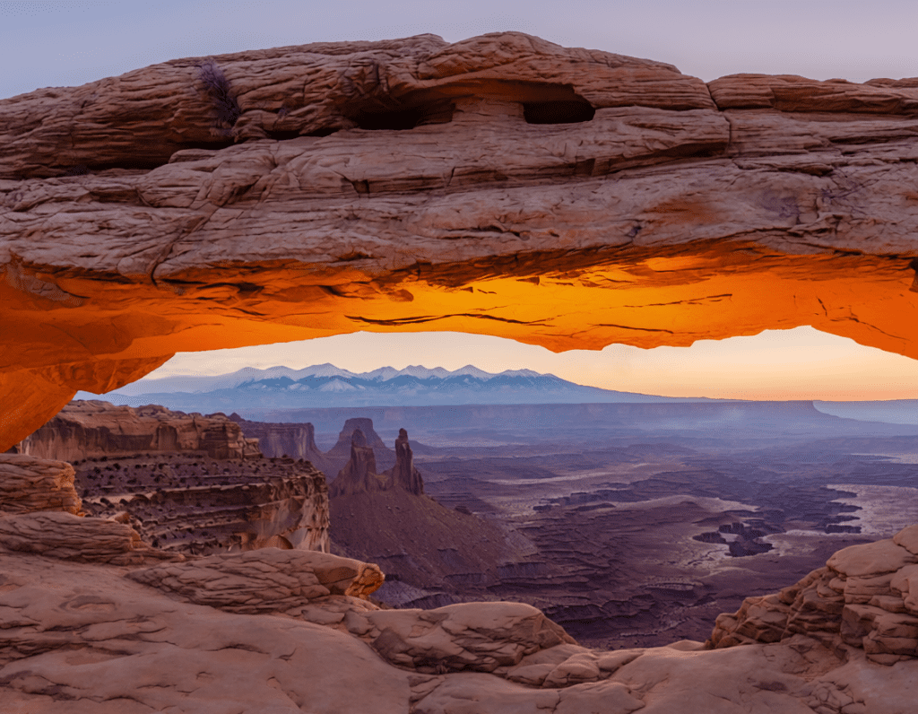 Mesa Arch Canyonlands National Park at sunrise, sandstone arch framing canyon below with reflected orange-gold sunrise glow illuminating underside of arch from canyon walls below
